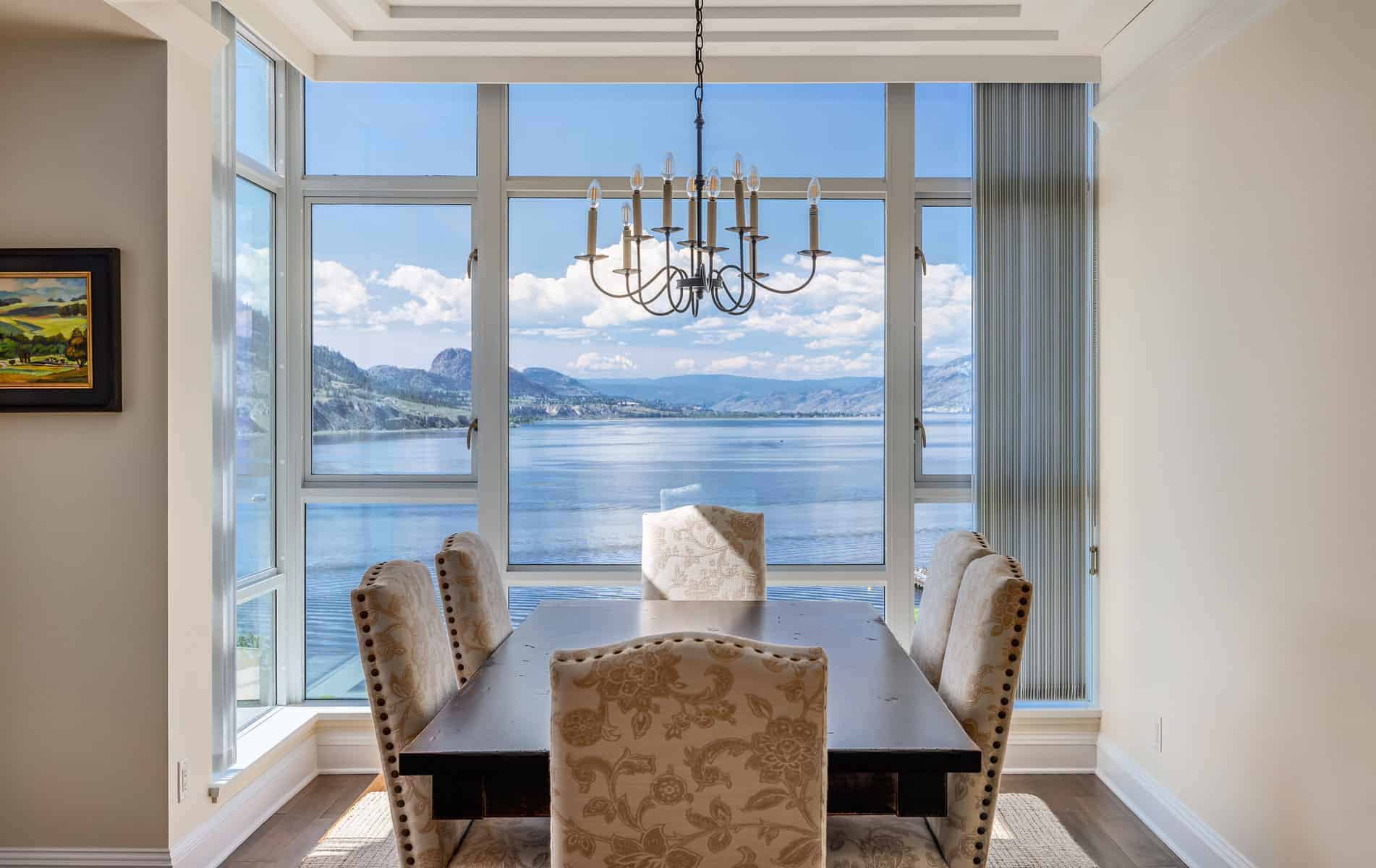 Formal dining room with a dark brown wooden table and upholstered white printed chairs with tall glass windows overlooking the ocean
