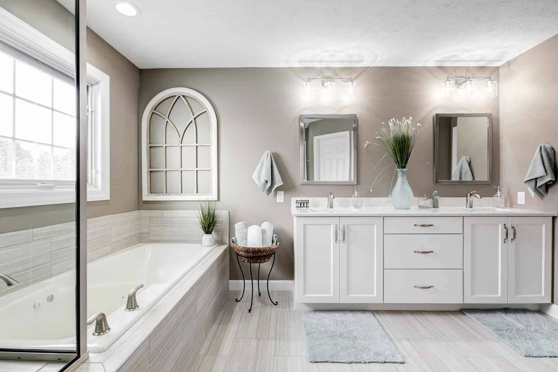 Master bathroom with cream interiors complete with a bathtub and twin mirror and wide wooden cabinet