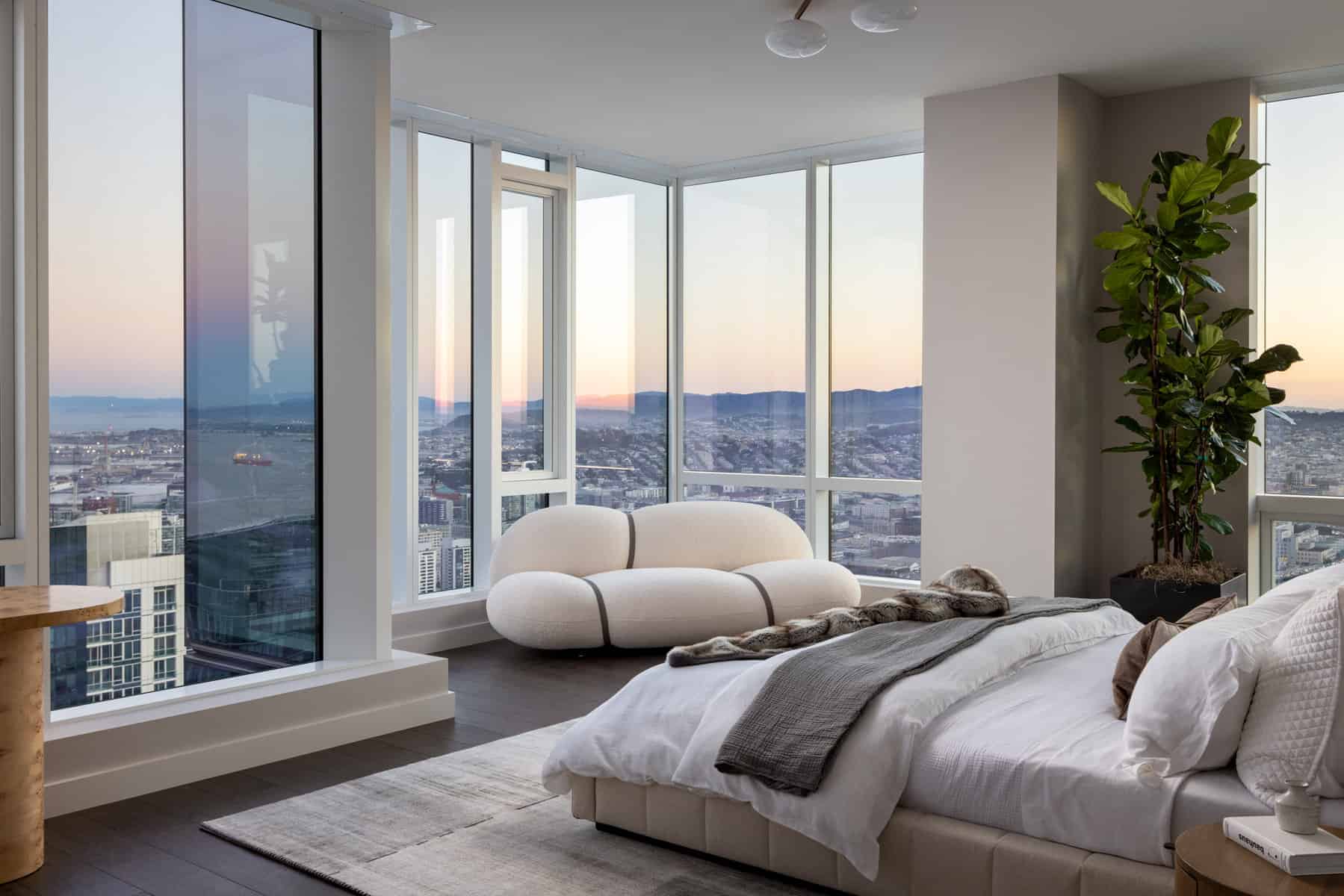 Condo bedroom with tall clear glass windows that showcases a white interior and white furnishings