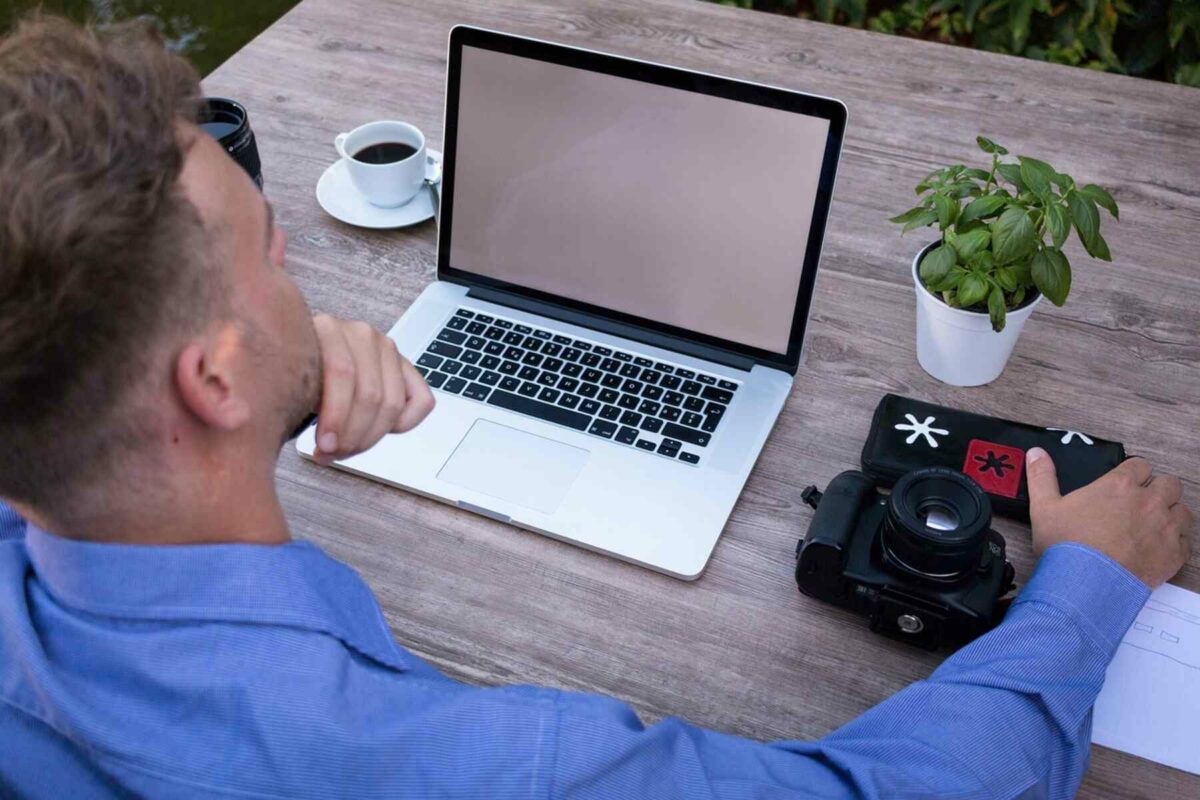 A man looking at his laptop with a DSLR camera beside it